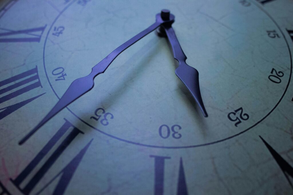 Detailed close-up of a vintage clock face with Roman numerals, focusing on the decorative hands at 30 past.